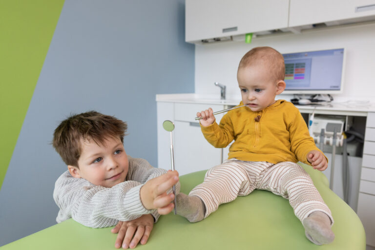 Junge mit Mundspiegel und Baby auf der Behandlungsliege in der Kinderzahnarztpraxis am Ostpark in München-Neuperlach